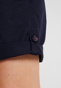 Mörkblå bomullsshorts med uppvikta fållar och knappdetalj med röd accent. Slät textur och skräddarsydd design för en ren passform.