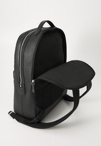 Sac à dos noir texturé avec une poignée supérieure et une fermeture éclair principale ouverte, montrant un dos rembourré et des bretelles réglables.