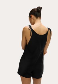 Jumpsuit nero senza maniche con spalline regolabili, schiena a scollo rotondo e vestibilità rilassata, realizzato in tessuto leggero.