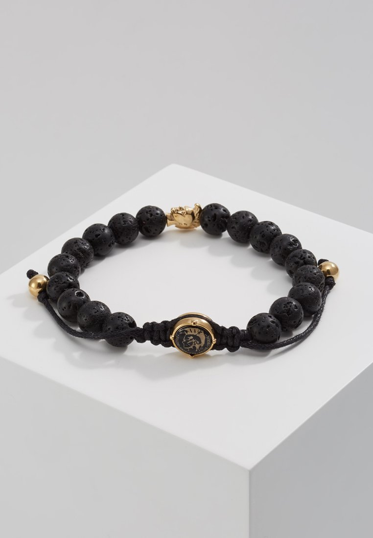 Armband aus schwarzem Lavastein mit einer goldfarbenen Verschluss- und Akzentfarbe. Verfügt über ein geflochtenes Band und einen dekorativen Charme in der Mitte.
