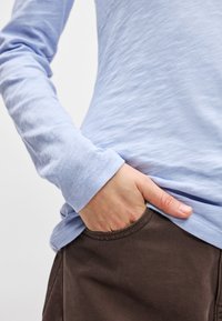 Svetlomodrá košeľa s dlhým rukávom a hladkou textúrou, v kombinácii s tmavohnedými nohavicami s prednou kapsou. Jednoduchý dizajn, žiadne viditeľné vzory.