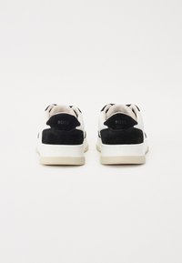 Black and white sneakers with suede and leather material. Features a rounded toe, thick sole, and embossed logo on the heel.