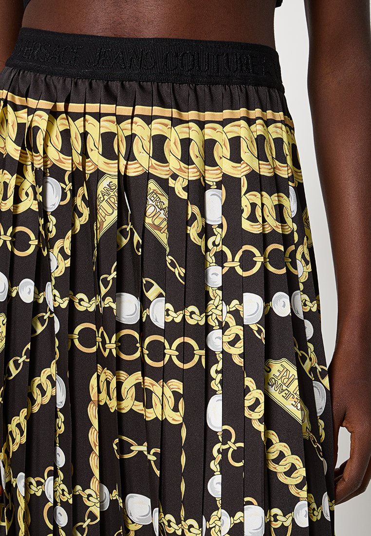 Jupe plissée noire avec chaîne dorée et motif en perles blanches, dotée d'une ceinture texturée avec un logo.