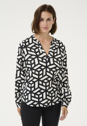 Blouse à manches longues noir et blanc avec un motif de cubes géométriques, présentant un décolleté en V et des poignets froncés. Texture semblable à de la soie.