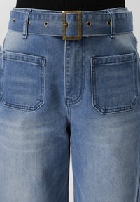 Džíny z lehkého modrého denimu s vysokým pasem, velkými předními nášivkovými kapsami a širokým páskem z téhož denimu s obdélníkovou mosaznou sponou.