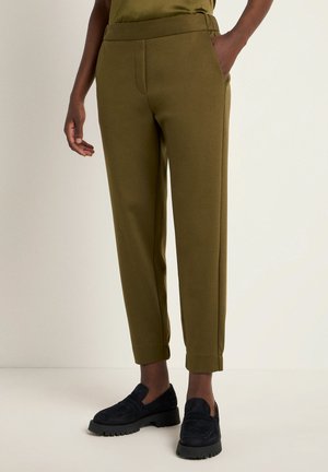 Olive green tapered trousers with a smooth texture, elastic waistband, and side pockets, paired with dark slip-on shoes.