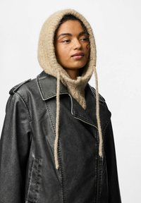 Jachetă biker din piele neagră cu rever larg, asociată cu un hanorac din tricot texturat de culoare bej deschis, având șnururi lungi.