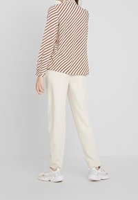 Striped blouse in cream and red, with long sleeves and a collar, paired with light-colored trousers and white sneakers.