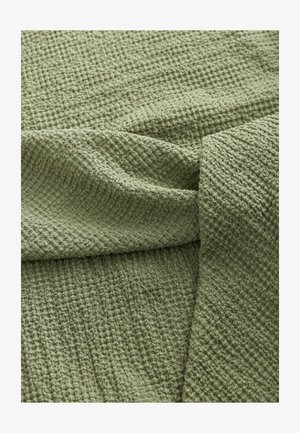 Tessuto verde texturizzato con una trama a motivi, caratterizzato da un aspetto morbido e increspato. Il materiale cade dolcemente con pieghe visibili.