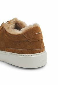 Brązowe zamszowe tenisówki z beżowym futerkiem i białą gumową podeszwą, z wytłoczonym logo "BOSS" na pięcie.