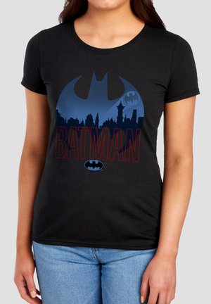 Woman wearing a black t-shirt with a blue Batman logo, city skyline silhouette, and red outline text reading "BATMAN" on the front.