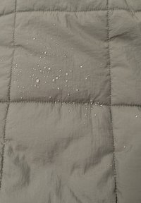 Manta gris acolchada con una superficie texturizada, con gotas de agua esparcidas por la tela, destacando su calidad resistente al agua.