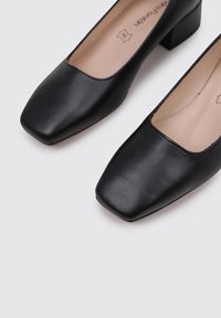 Chaussures en cuir noir à talons carrés avec un design à bout carré. Texture lisse avec une esthétique minimaliste et une doublure intérieure beige.
