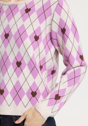 Personne portant un pull en maille à motif argyle rose, blanc et marron, avec des cœurs marron aux intersections des losanges.