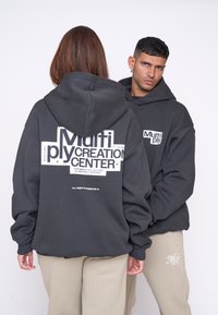 Sudaderas gris de gran tamaño con texto gr�áfico blanco en la parte delantera y trasera. Presenta una textura suave y un corte relajado, combinadas con pantalones beige claros.