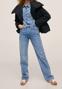 Blå denimskjorte og brede bukser med forlommer. Sort puffjakke lagdelt over. Fodtøj med lyserøde og hvide detaljer.