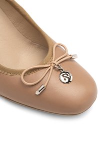 Beige bőr balettcipő, puha tapintással, szatén masnival és ezüst bájjal, valamint párnázott belső résszel a kényelem érdekében.