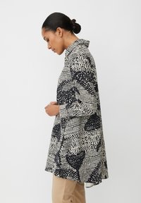 Langärmliges Hemd mit schwarz-weißem Muster und Kragen; enthält abstrakte Designs und einen leicht gewölbten Saum. Glatte Stofftextur.