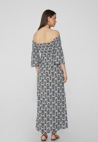 Un vestido maxi blanco y negro sin mangas con un patrón floral, mangas fluidas y un corsé ajustado con la parte trasera fruncida.