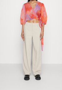 Top recortado con patrón de acuarela en naranja y rosa, combinado con pantalones de pierna ancha beige y zapatos de plataforma negros. Tela suave, ajuste holgado.