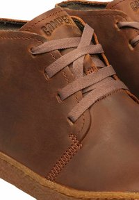 Zapatos casuales de cuero marrón con detalles de costura, cordones de tela y suelas de goma que presentan el nombre de la marca "Camper" en la lengüeta.