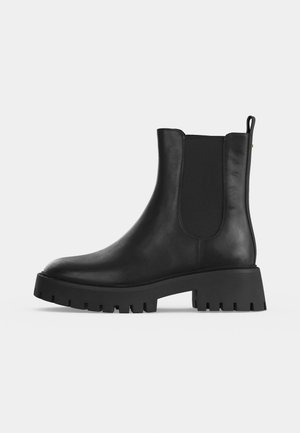 Black leather Chelsea boot with chunky lug sole, elastic side panel, and pull tab at the back, shown in profile view on a white background.