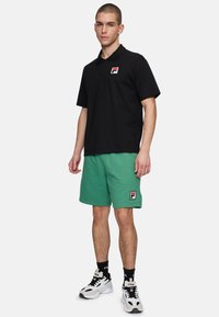 Svart pikétröja med en logotyp, gröna shorts och vita sneakers med svarta detaljer. Klädseln har en avslappnad passform och en avslappnad design.