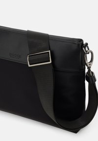 Borsa a spalla nera realizzata in nylon con una texture liscia, dotata di una fibbia in metallo argento e una tracolla regolabile. Logo impresso sul lato.