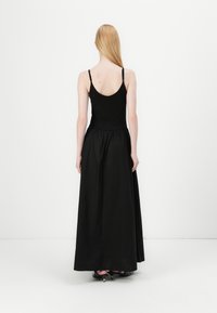 Μαύρο, χωρίς μανίκια φόρεμα με εφαρμοστό μπούστο και ρέουσα, μακρύς φούστα έως τον αστράγαλο. Λείο ύφασμα με μαζεμένη μέση και ελάχιστες λεπτομέρειες.