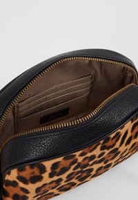 Kabelka s leopardím potiskem, černými koženými detaily, texturovaným povrchem, zlatým zipem a vnitřními přihrádkami na karty na podšívce s puntíky.