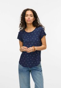 Marineblauw overhemd met korte mouwen, voorzien van een groen stippenpatroon, ronde halslijn en een afgeronde zoom. De stof lijkt lichtgewicht en soepel.