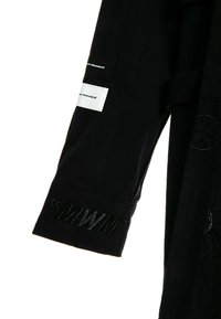 Prenda de color negro con mangas largas y detalles bordados en los puños. Presenta una etiqueta rectangular blanca con texto. Está hecha de una tela suave y tiene un diseño sencillo.