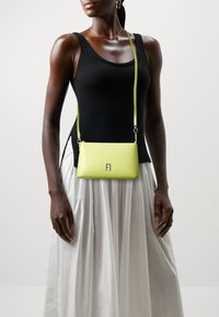 Piccola borsa a tracolla in pelle verde lime vibrante, forma rettangolare, con un accentuato logo metallico e una tracolla sottile.