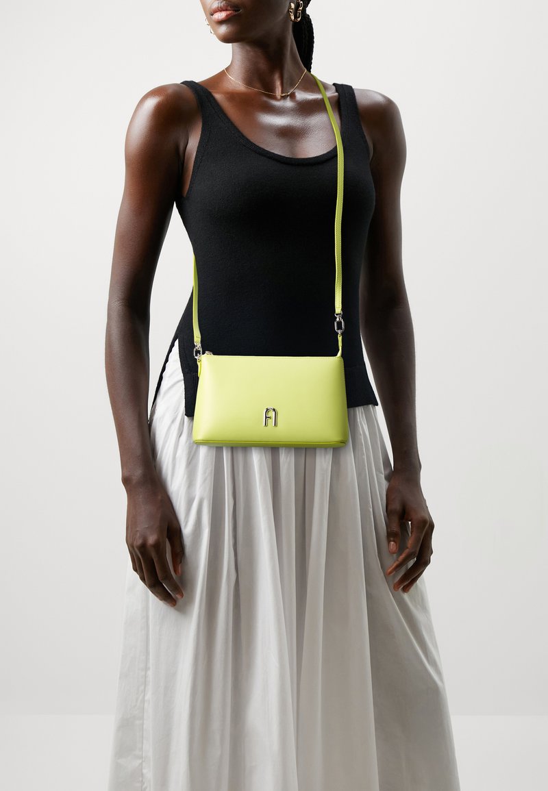 Piccola borsa a tracolla in pelle verde lime vibrante, forma rettangolare, con un accentuato logo metallico e una tracolla sottile.