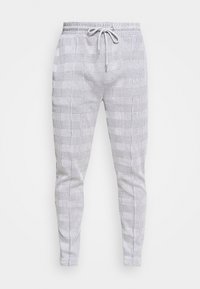 Grå och vit rutmönstrad joggingbyxor gjorda av ett lätt material. Har en elastisk midja med snodd och en avsmalnande ben-design.