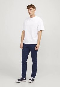 Hvit bomulls-T-skjorte med korte ermer, kombinert med mørkeblå bukser. Antrekket kompletteres med marineblå sneakers med hvite såler.