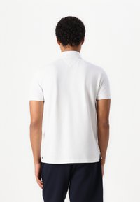 White short-sleeve polo shirt featuring a classic collar, textured fabric, and side vents, paired with navy pants.