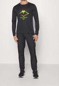 Pitkähihaisa musta urheilupaita, jossa on keltainen kolmiomainen vuorikuvio ja "FUJITRAIL"-teksti, yhdistettynä mustiin housuihin ja mustiin lenkkitossuihin.