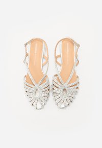 Sandales argentées à lanières avec un design tissé et une ouverture sur l'avant. Elles possèdent une bride de cheville et une semelle intérieure beige clair. Semelle plate.