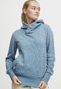 Sudadera azul claro con cuello tipo cowl, tres botones y un patrón de pequeños círculos en rosa y blanco. Incluye detalles de puños y dobladillo acanalados.