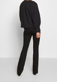 Haut noir à manches longues avec encolure froncée et manches texturées, associé à un pantalon noir évasé et ajusté. Les deux vêtements ont une finition lisse.