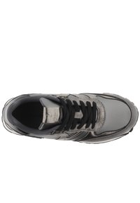 Zapatilla atlética gris con parte superior texturizada, cordones negros, cuello acolchado y acentos en contraste. Presenta un diseño de punta redondeada y elegante.