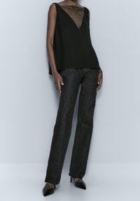 Haut noir sans manches avec un décolleté en V et des détails en mesh, associé à un jean foncé et des escarpins noirs pointus. Design simple et épuré avec une silhouette moderne.