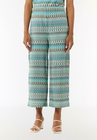 Pantalons courts amples présentant un motif ondulé teal et blanc avec des accents marron. Fabriqués en tissu léger, texture lisse.