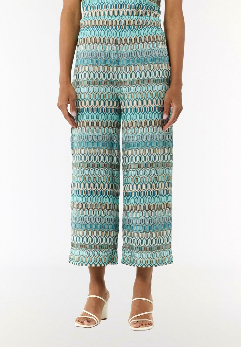 Pantalons courts amples présentant un motif ondulé teal et blanc avec des accents marron. Fabriqués en tissu léger, texture lisse.