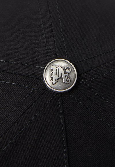 Black cap featuring a textured fabric, stitched details, and a prominent metallic button with stylized initials in the center.