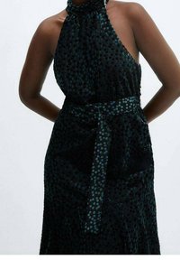 Schwarzes Kleid mit einem Halterneck, aus strukturiertem Stoff mit tealfarbenen Punkten, gebundenem Taillenbund und fließender Silhouette.