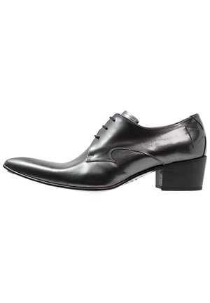 Zapato de vestir de cuero negro pulido con punta puntiaguda, cierre de cordones y tacón de bloque apilado, mostrado desde una vista lateral.