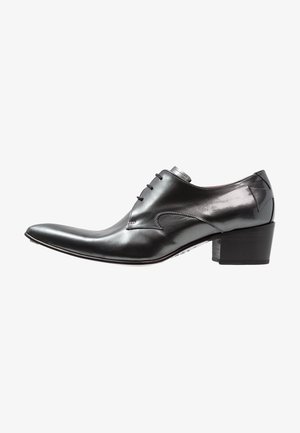 Zapato de vestir de cuero negro pulido con punta puntiaguda, cierre de cordones y tacón de bloque apilado, mostrado desde una vista lateral.