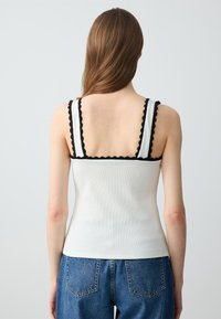 Top in cotone bianco a costine con spalline nere a scallop, design aderente e schiena liscia. Abbinato a jeans in denim blu a vita alta.